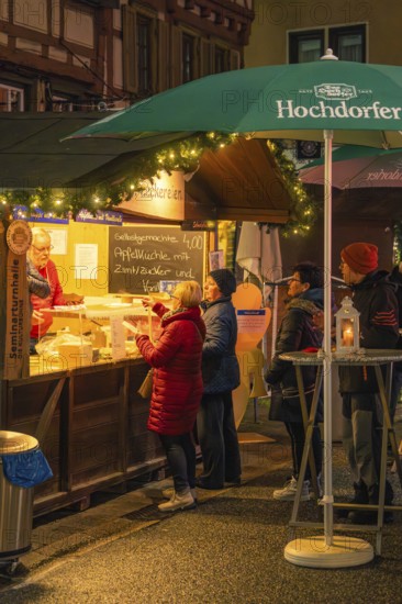 People stand at a well-lit stand to buy pastries at a Christmas market, Christmas market 2025, Nagold, Black Forest, Calw district, Germany