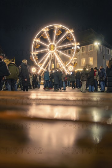 People enjoy the illuminated Ferris wheel on a cobblestone square at night, Christmas market 2025, Nagold, Black Forest, Calw district, Germany