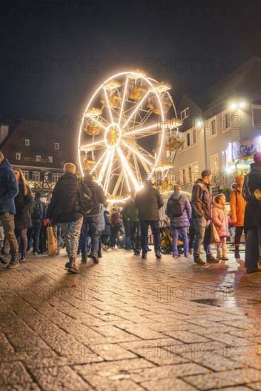 People walk across a square with illuminated Ferris wheel at night, Christmas market 2025, Nagold, Black Forest, Calw district, Germany