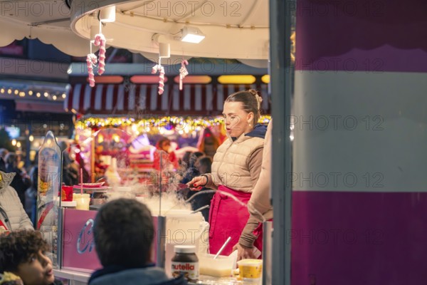 A woman cooks at a market stall surrounded by steaming food and colorful light, Christmas market 2025, Nagold, Black Forest, Calw district, Germany