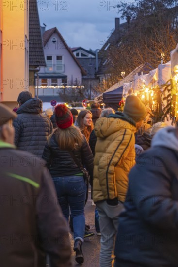 Visitors to a busy market stroll through festive lighting, Aidlingen Christmas Market, Böblingen District, Germany