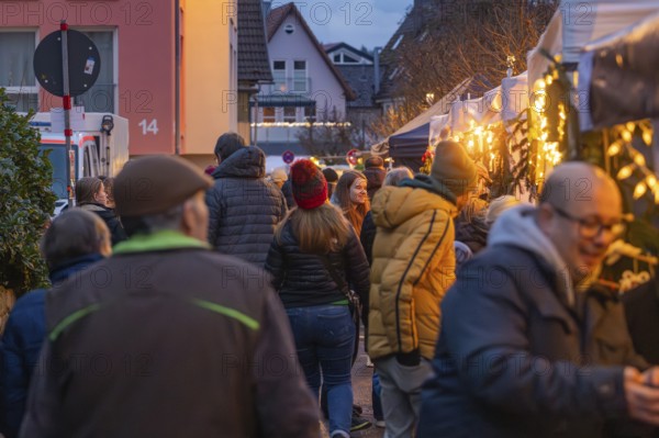 People stroll through an illuminated night market in a street, Aidlingen Christmas market, Böblingen district, Germany