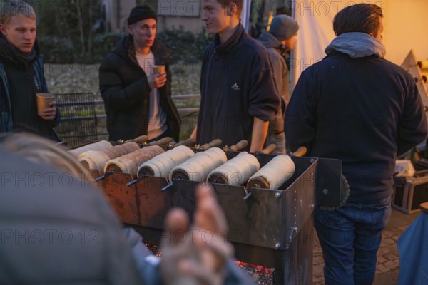 Vendors at a stand at a Christmas market prepare traditional tree striezel under evening lighting, Aidlingen Christmas market, Böblingen district, Germany