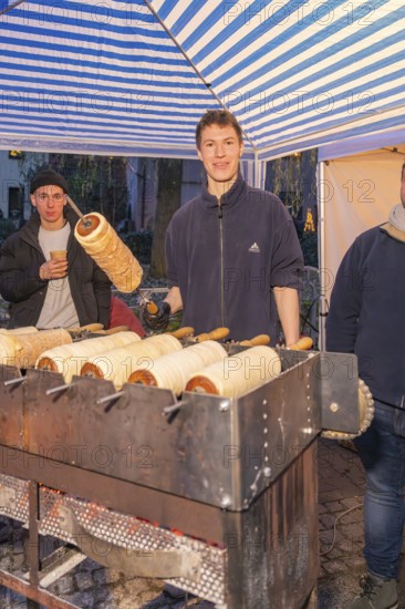 A market stand selling tree strips. A smiling person shows a tree striezel, Aidlingen Christmas market, Böblingen district, Germany