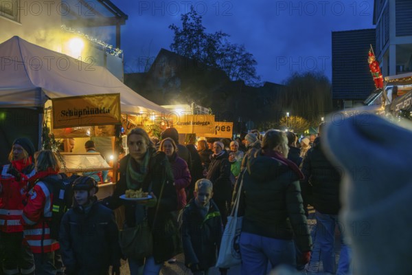Families and children stroll through festively lit food stalls at a Christmas market in the evening, Aidlingen Christmas market, Böblingen district, Germany