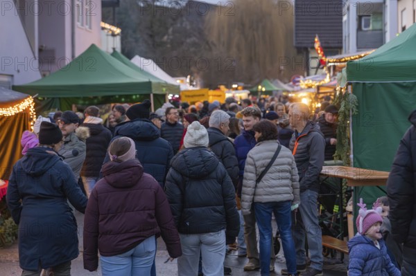 A crowd of people moves through a Christmas market with brightly decorated stalls, Aidlingen Christmas market, Böblingen district, Germany