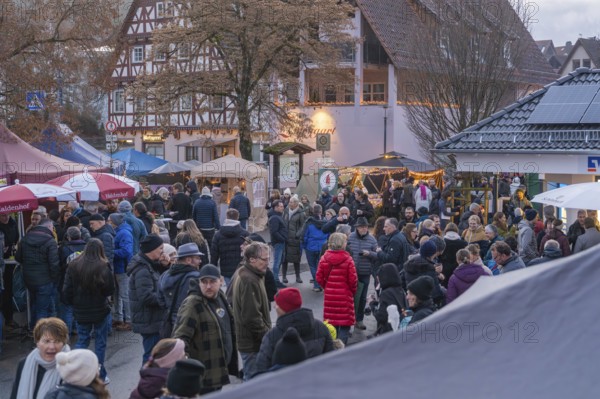 Lively Christmas market in front of half-timbered houses and trees, numerous visitors enjoy the evening mood, Aidlingen Christmas market, Böblingen district, Germany