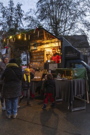 An illuminated food truck at a street market with people in a nocturnal atmosphere, Aidlingen Christmas market, Böblingen district, Germany