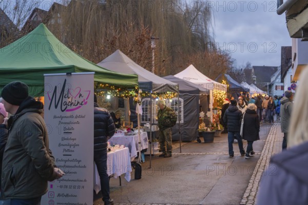 People stroll through a market with various illuminated stands in the evening, Aidlingen Christmas market, Böblingen district, Germany