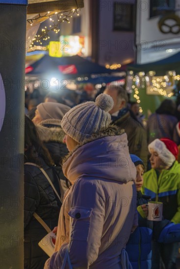 Woman in warm winter clothes holding coffee cup surrounded by children and twinkling lights at the market, Aidlingen Christmas market, Böblingen district, Germany