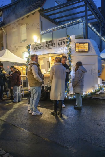 Friends chatting in front of an illuminated beverage stand at night, Aidlingen Christmas Market, Böblingen District, Germany