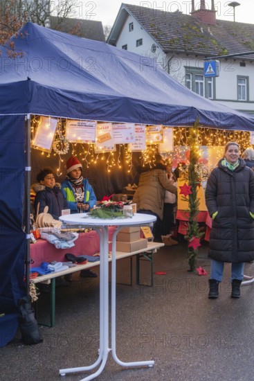 People stand at a decorated market stand under a tent at a busy Christmas market, Aidlingen Christmas market, Böblingen district, Germany