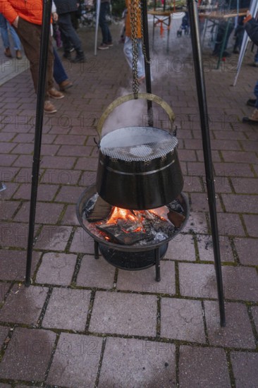 A cauldron hangs over a glowing fire on outdoor cobblestones at a Christmas market, Aidlingen Christmas market, Böblingen district, Germany