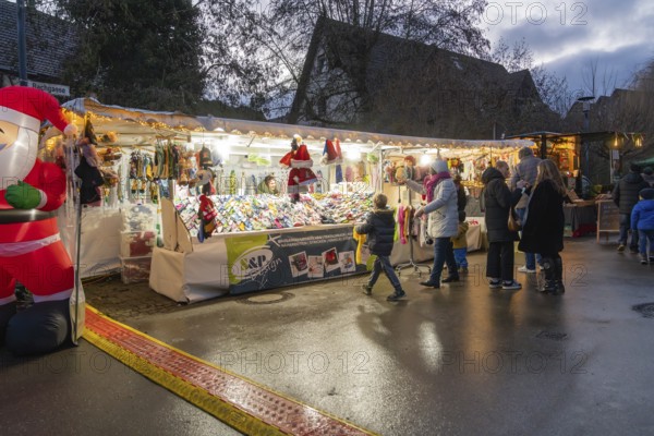 People stand at an illuminated Christmas market stand with decorations at dusk, Aidlingen Christmas market, Böblingen district, Germany