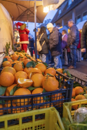 Fresh oranges in boxes in front of curious market visitors in the evening, Aidlingen Christmas market, Böblingen district, Germany