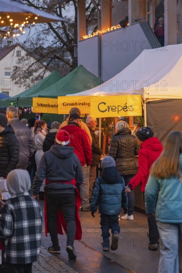 Visitors stroll along illuminated stands at an evening market, Aidlingen Christmas Market, Böblingen District, Germany
