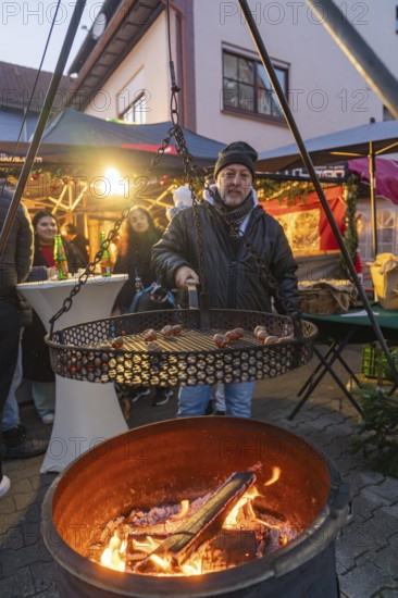 Man grilling chestnuts at a Christmas market in a pleasant evening mood, Aidlingen Christmas market, Böblingen district, Germany