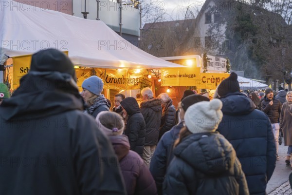 People wearing winter clothes in front of illuminated food stalls at a market, Aidlingen Christmas market, Böblingen district, Germany