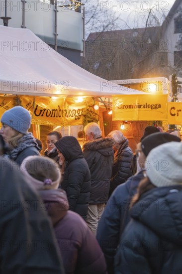 People stand at a brightly lit stand at a Christmas market, wrapped in warm clothes, Aidlingen Christmas market, Böblingen district, Germany