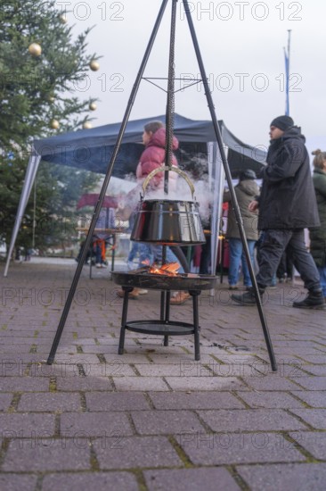 A cauldron over an open fire at a Christmas market with people and Christmas decorations, Aidlingen Christmas market, Böblingen district, Germany