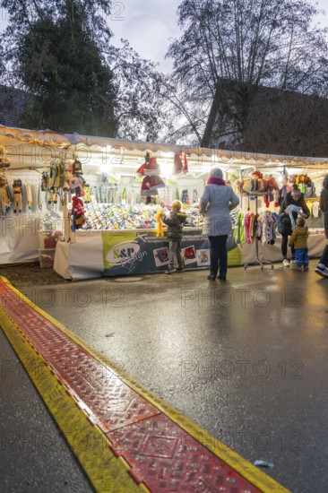 A market stall at dusk with people looking at goods while it rains, Aidlingen Christmas market, Böblingen district, Germany