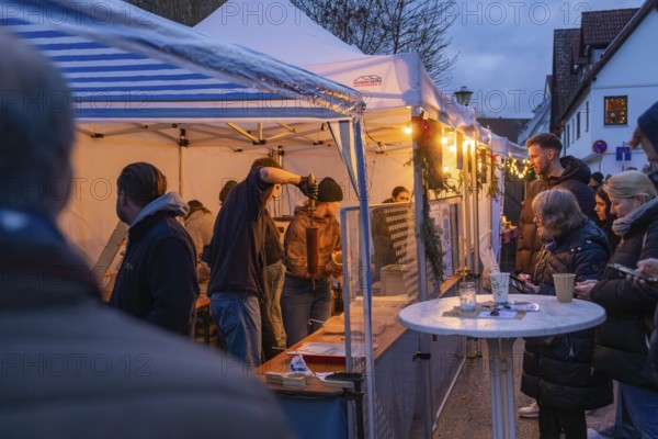 People at a market stand at dusk enjoying the festive atmosphere, Aidlingen Christmas Market, Böblingen District, Germany
