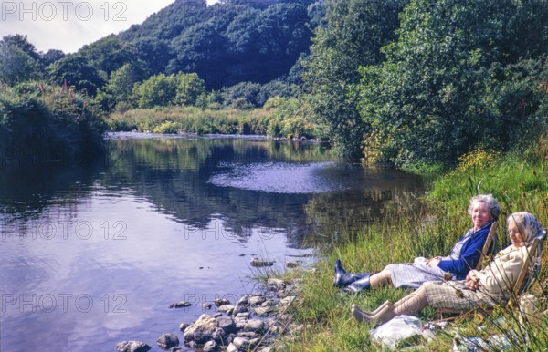 Two women sitting in deckchairs by the side of River Nevern, Penwaun, Nevern, Pembrokeshire, Wales, UK 12 July 1971