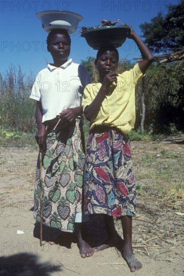 Two local woman balance bowls on their heads and pose for the camera at Kande on Lake Malawi, Malawi, Africa, July 2000, vintage, retro, old, historic