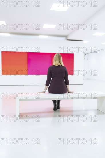 A woman sits in a modern, white art gallery and looks at a large, colorful painting, Open Horizons exhibition, Schauwerk Sindelfingen, BÃ¶blingen district, Germany