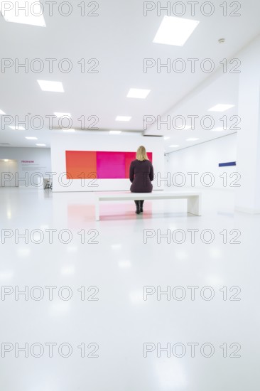 White minimalistic room with woman on a bench in front of colored painting, Open Horizons exhibition, Schauwerk Sindelfingen, BÃ¶blingen district, Germany