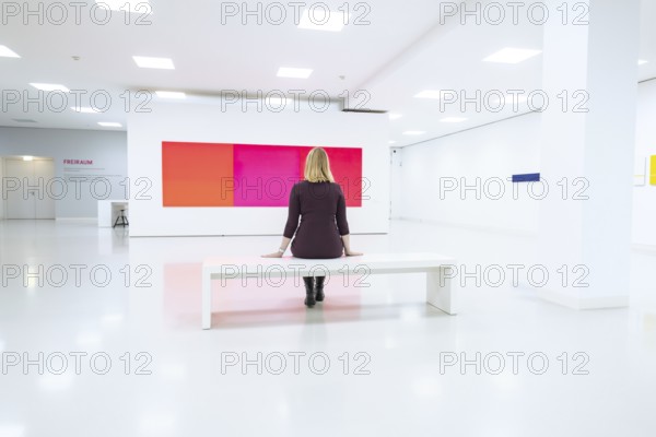 A woman sits alone on a bench in a bright white art gallery, Open Horizons exhibition, Schauwerk Sindelfingen, BÃ¶blingen district, Germany