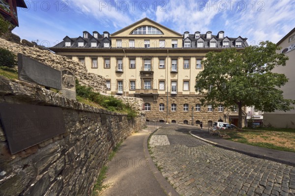 Sandstone wall, historic building, house, faÃ§ade with windows, dormers, asphalt sidewalk, cobblestone street, trees, meadow, blue sky, altocumulus clouds, cirrus clouds, street Am Römertor, Wiesbaden, state capital, district-free city, Hesse, Germany