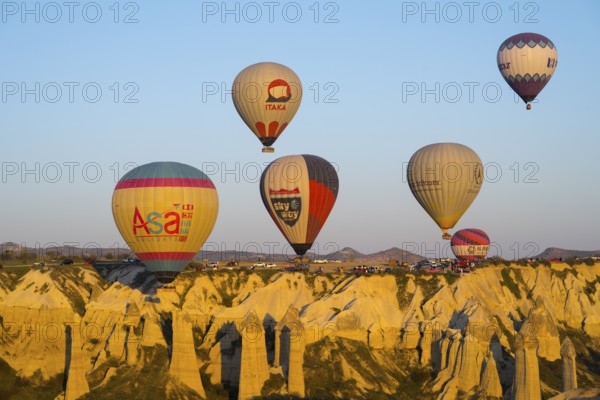 Balloons with logos floating over a rocky landscape with mountain views in the background, hot air balloons, Göreme National Park, Göreme Tarihî Millî Park, Nevsehir Province, NevÅŸehir, Cappadocia, Cappadocia, Central Anatolia, Turkey