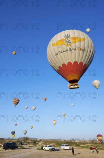 Hot air balloons rise from a meadow while people and cars are on the ground, Göreme National Park, Göreme Tarihî Millî Park, Nevsehir Province, NevÅŸehir, Cappadocia, Capadocia, Central Anatolia, Turkey