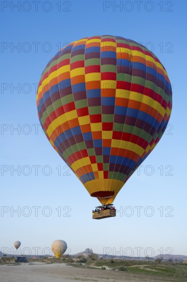A colorful hot air balloon floats in daylight over a meadow under clear blue sky, Göreme National Park, Göreme Tarihî Millî Parki, Nevsehir Province, Nevsehir, Cappadocia, Cappadocia, Central Anatolia, Turkey
