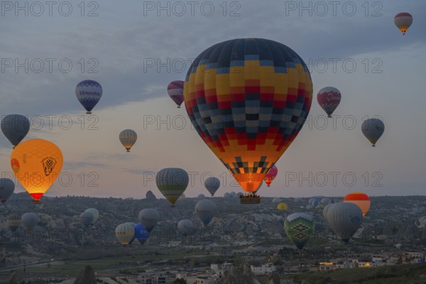 Colourfully patterned hot air balloons rise over the city and countryside of Cappadocia, Göreme National Park, Göreme Tarihî Millî Parki, Nevsehir Province, Nevsehir, Cappadocia, Cappadocia, Central Anatolia, Turkey