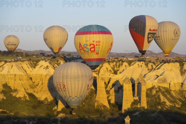 A group of balloons floats along a sunlit rock formation, hot air balloons, Göreme National Park, Göreme Tarihî Millî ParkÄ±, Nevsehir Province, Nevsehir, Cappadocia, Cappadocia, Central Anatolia, Turkey