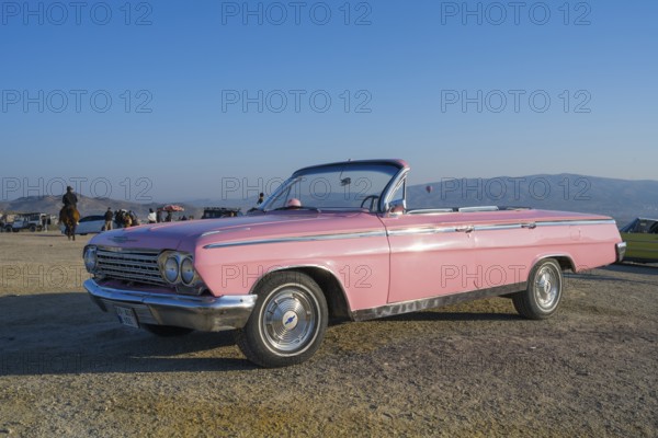 A pink vintage convertible car stands in a vast landscape with mountains in the background and blue sky, Chevrolet, Göreme National Park, Göreme Tarihî Millî ParkÄ±, Nevsehir Province, NevÅŸehir, Cappadocia, Cappadocia, Central Anatolia, Turkey