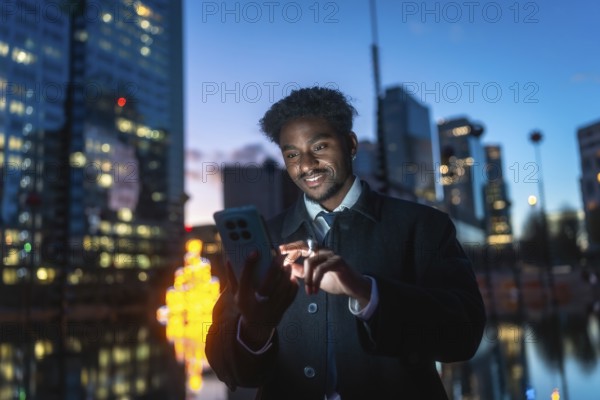 Young man standing outdoors at night, smiling while interacting with a smartphone, reflecting modern communication, global connectivity, and the digital lifestyle within a busy city environment