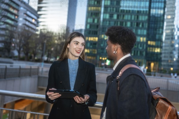 Business colleagues having a productive outdoor meeting, discussing work while holding a tablet in a modern urban district with office buildings and clear sky