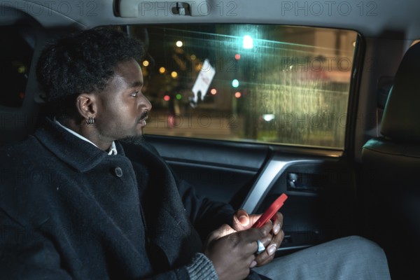 Afro american passenger riding in a car, looking out the window at city lights while holding a smartphone, capturing moments of urban public or private transport journey