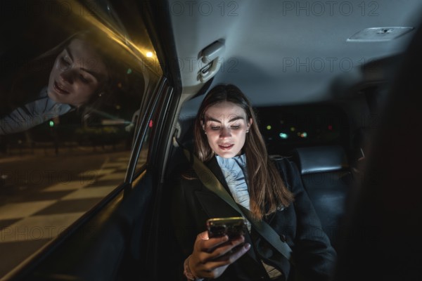 Young businesswoman in backseat at night, focused on smartphone screen while commuting through illuminated city streets, reflecting street lights and digital connection