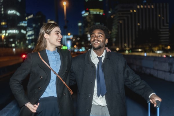 Diverse business colleagues smiling and walking together carrying luggage in an urban setting at night, representing successful travel, partnership, and global business connections