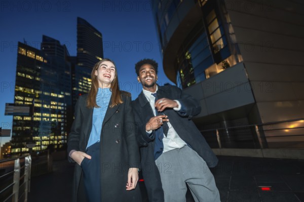 Diverse businesspeople enjoying a joyful moment together while standing on a promenade with illuminated city skyscrapers in the background during a vivid evening