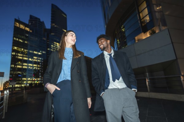 Diverse business professionals sharing a cheerful moment, smiling and talking under the city lights at night, representing successful communication and partnership in a modern urban environment