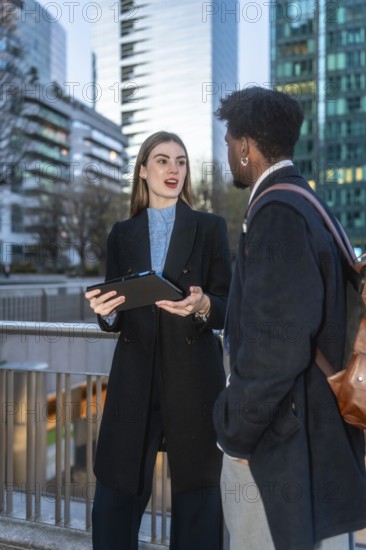 Business professionals collaborating outdoors, reviewing data on a tablet in an urban setting, representing modern work environments, technology, and diverse teams in a cityscape background