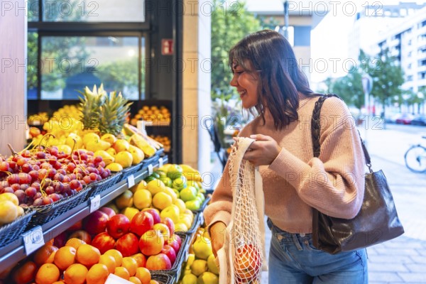 Smiling woman browsing and selecting fresh organic fruit from a display stand in a modern supermarket, placing produce into her eco friendly string shopping bag