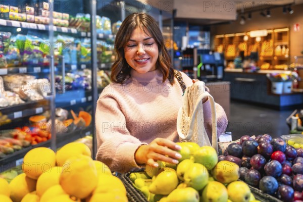 Young woman in a supermarket produce aisle selects ripe pears, carrying a reusable string bag for eco friendly grocery shopping and sustainable, healthy food choices