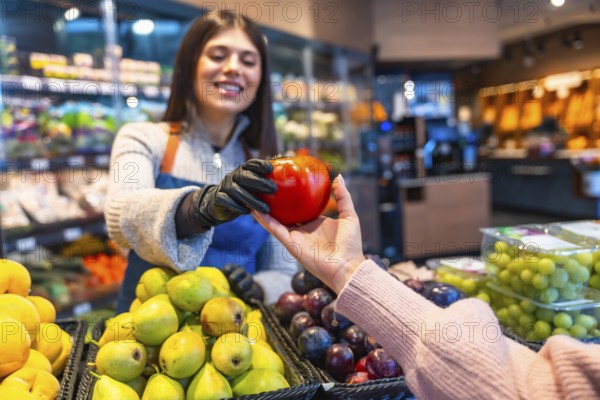 Greengrocer providing customer with a fresh organic tomato, emphasizing quality service and healthy food choices in a modern grocery store or market setting