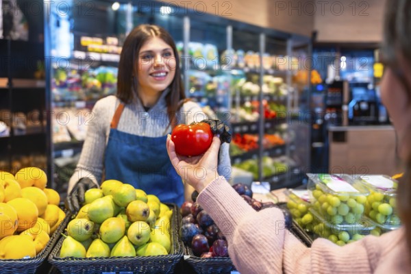 Greengrocer handing a ripe red tomato to a customer during grocery shopping in a produce section, showing excellent store service and healthy food choices